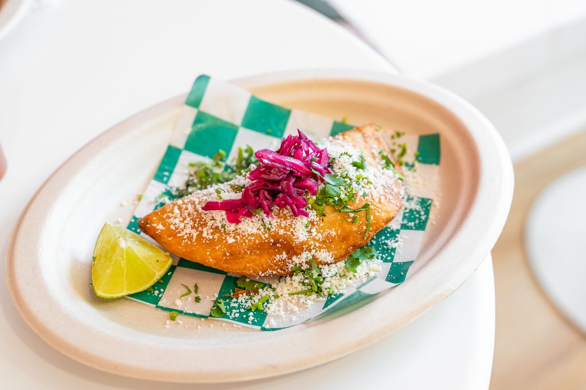 An empanada topped with pickled red cabbage on a white plate. 