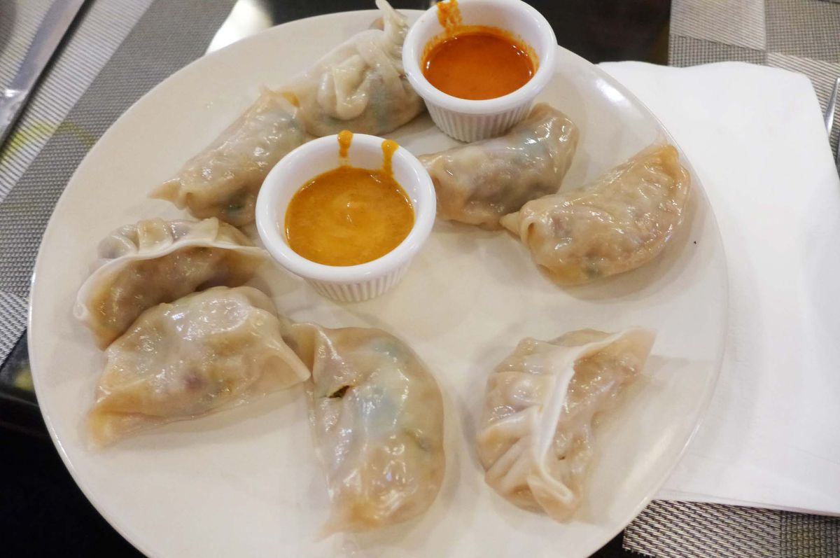 Eight dumplings with orange and red sauces on the side.