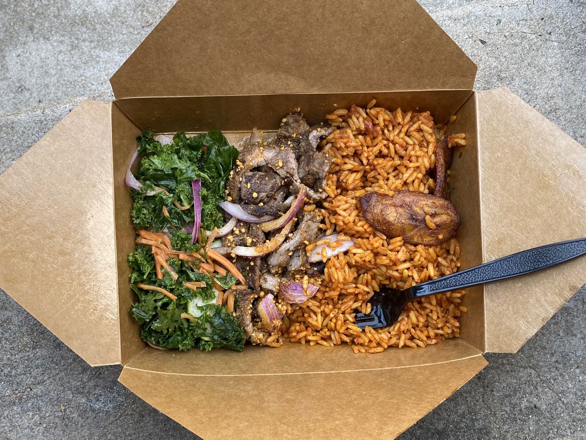 An overhead photograph of a takeout container of beef suya, kale salad, and jollof rice.