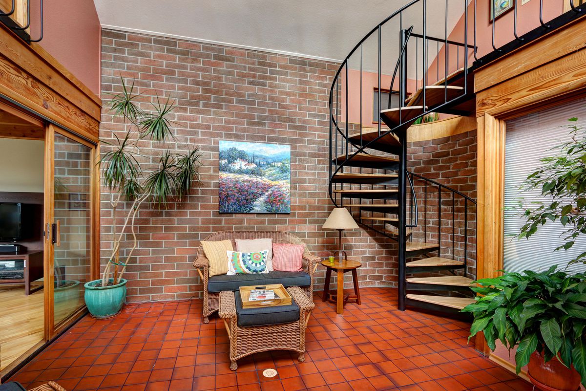 Tiled brick floor and brick accent wall in atrium with spiral staircase to right and wood frame sliding glass door to left