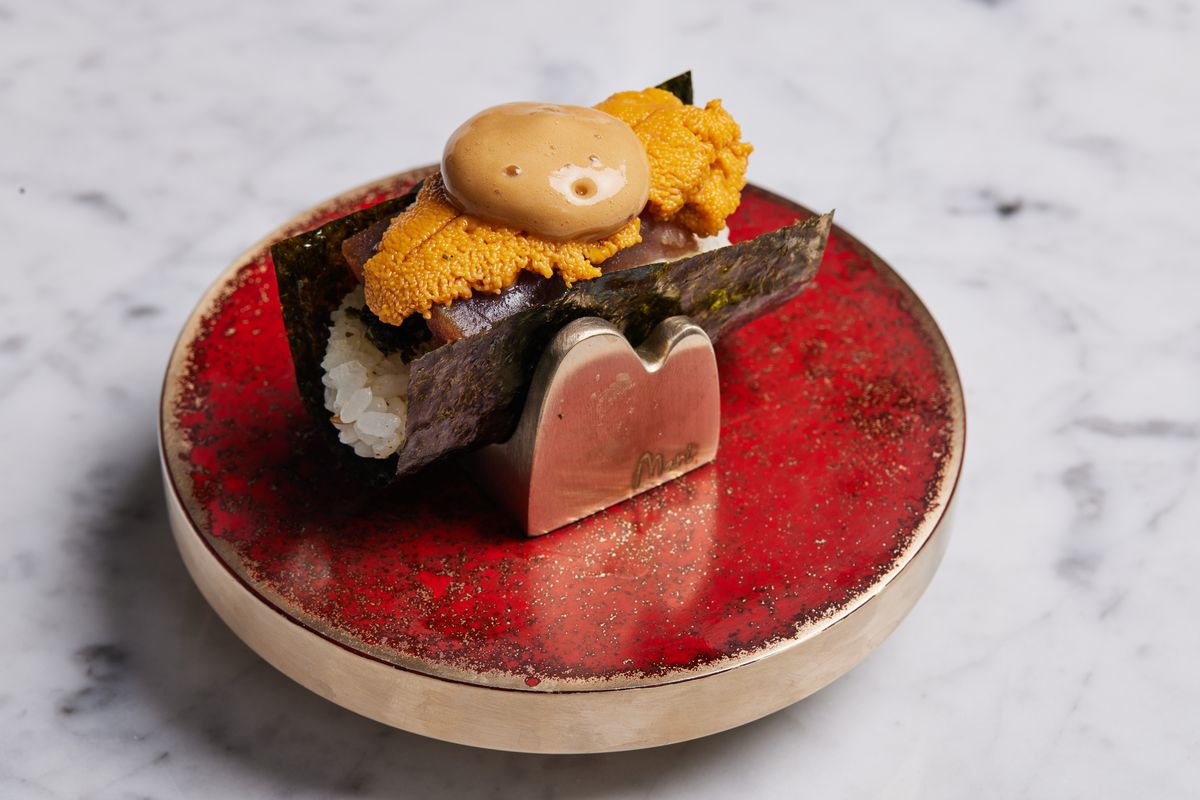 Uni lies above tuna in this hand roll, which sits on an ornamental red holder