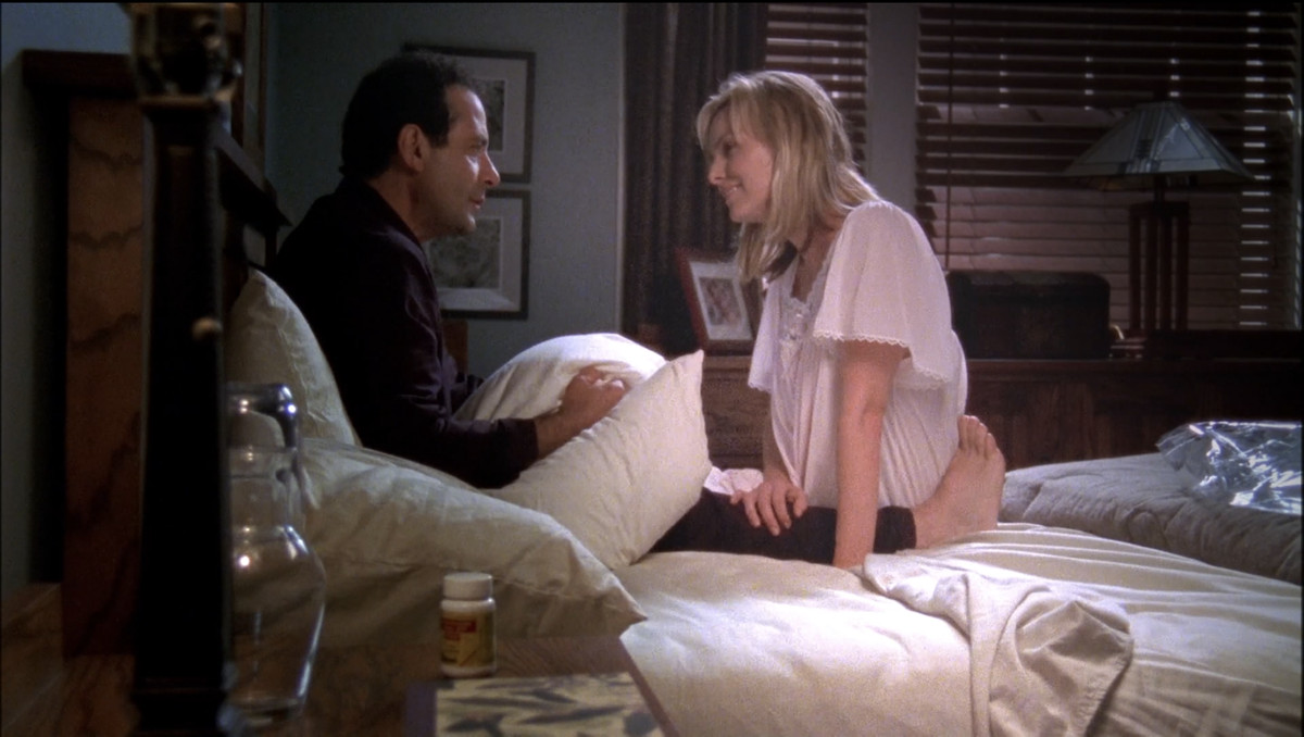 Monk (Tony Shalhoub) holding Trudy’s pillow and looking sad while her ghost (Melora Hardin) sits in front of him smiling