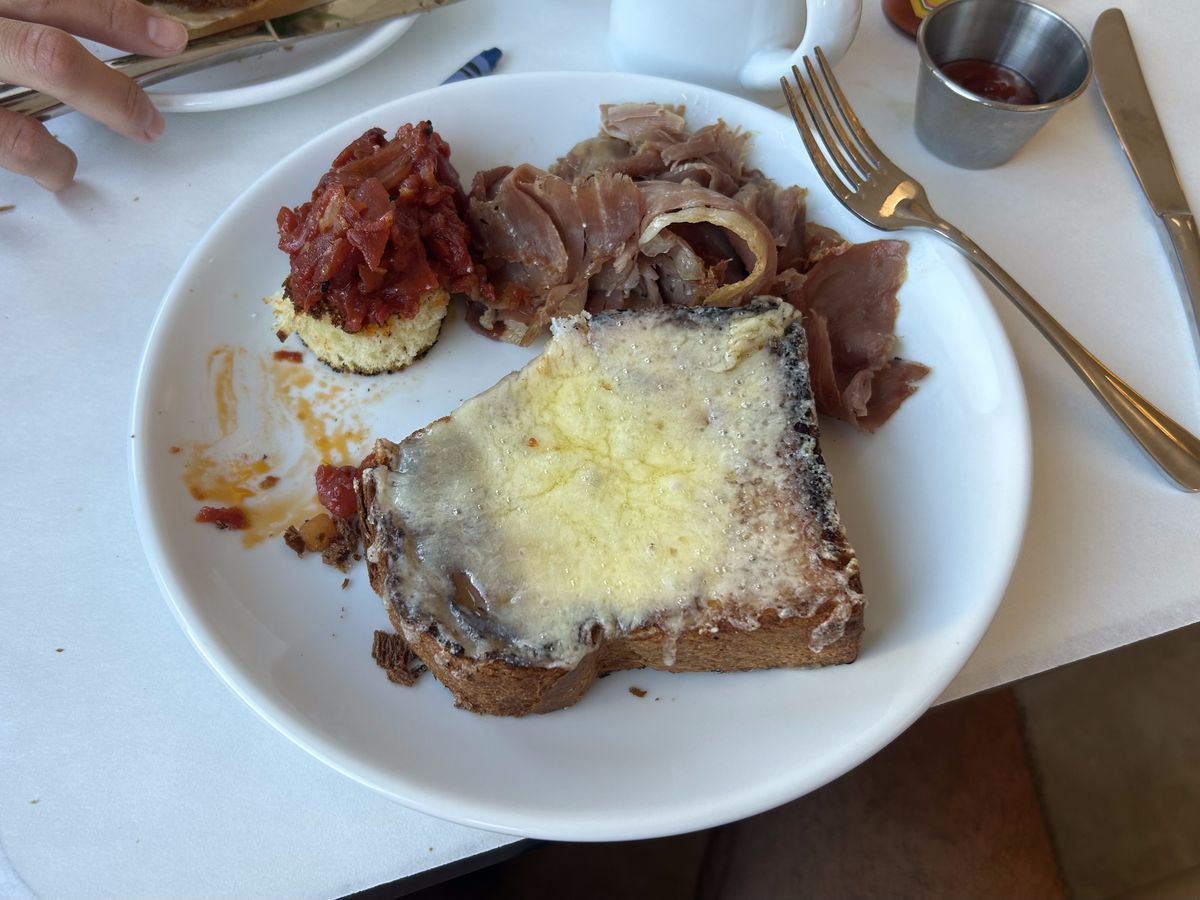 A slice of brioche bread is topped with melted cheese and served with a side of country ham.
