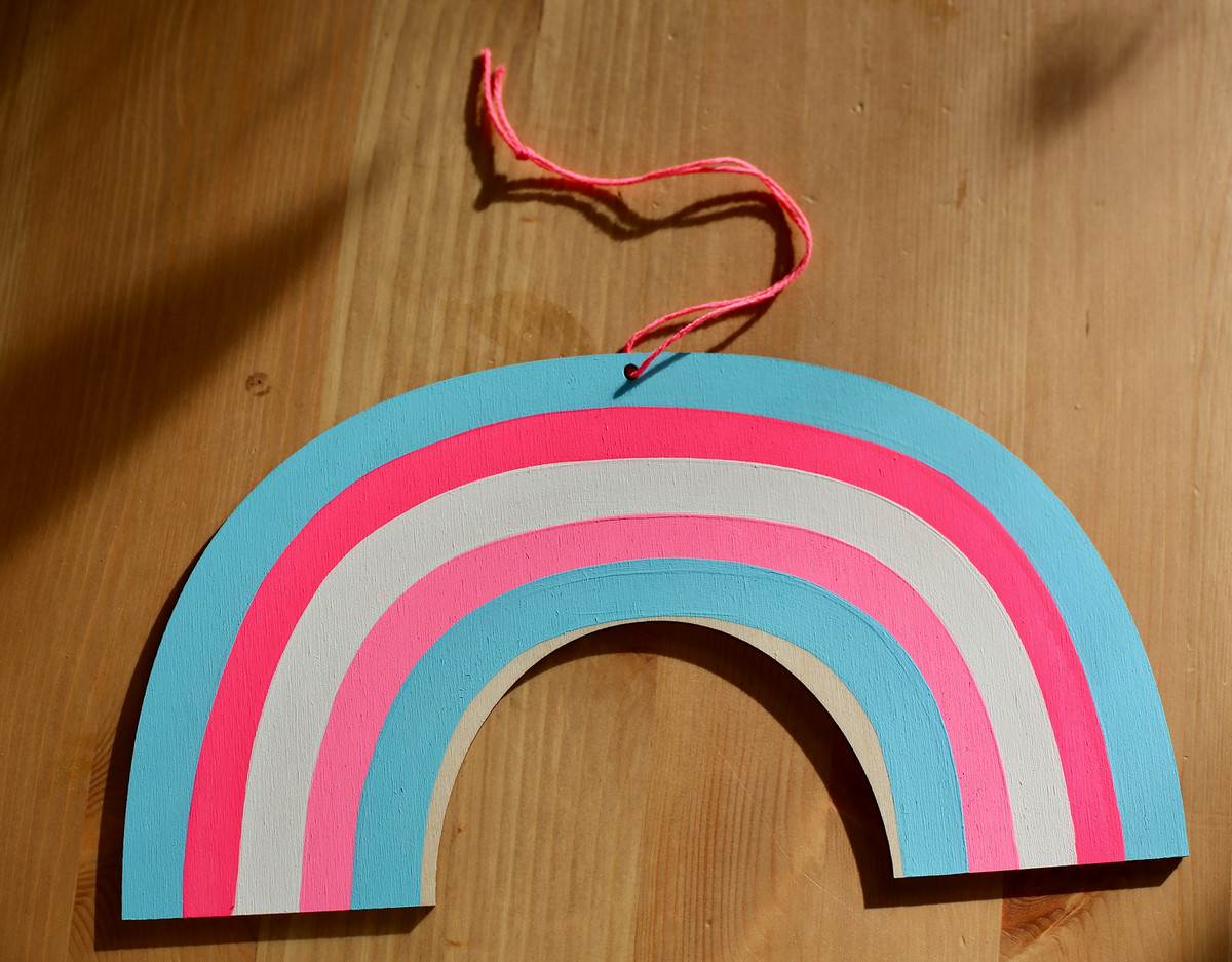 A wooden window charm shaped like a window with the colors of the trans rights flag.