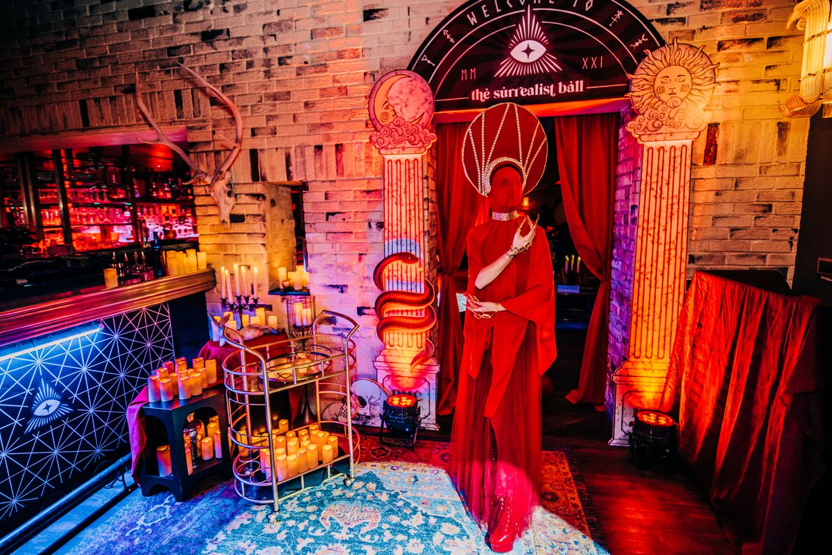 A performer in red in front of a witchy candle-lit setup.