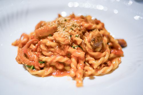 A white bowl with fusilli, red sauce, bone marrow, and octopus.