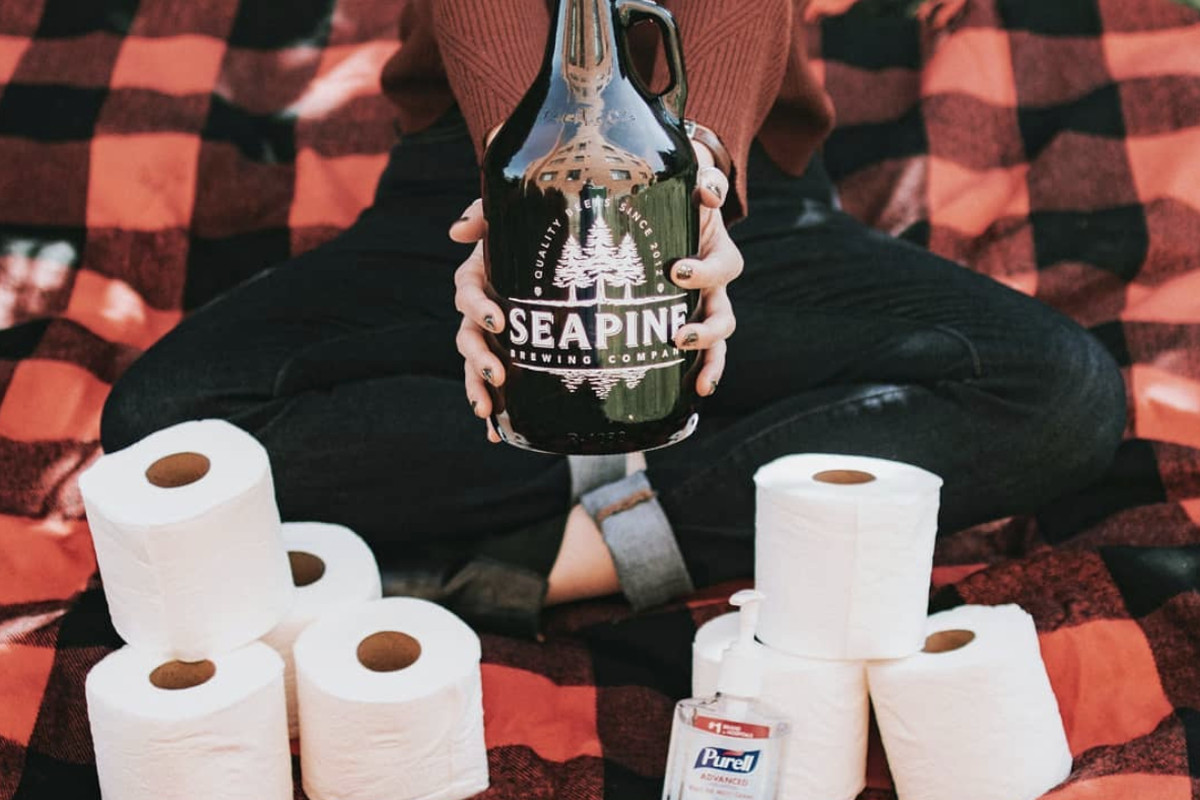 A woman holding a Seapine Brewing growler surrounded by toilet paper and Purrell.