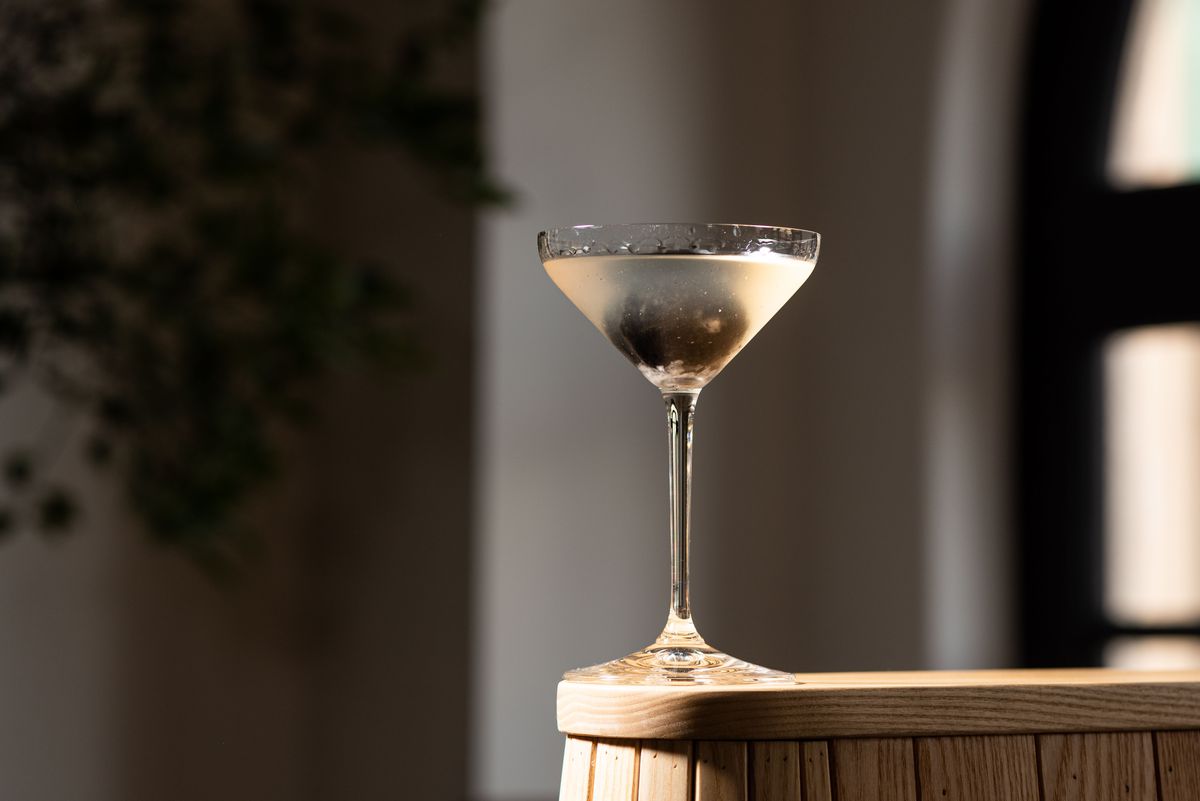 A martini with dark ice at the edge of a table.