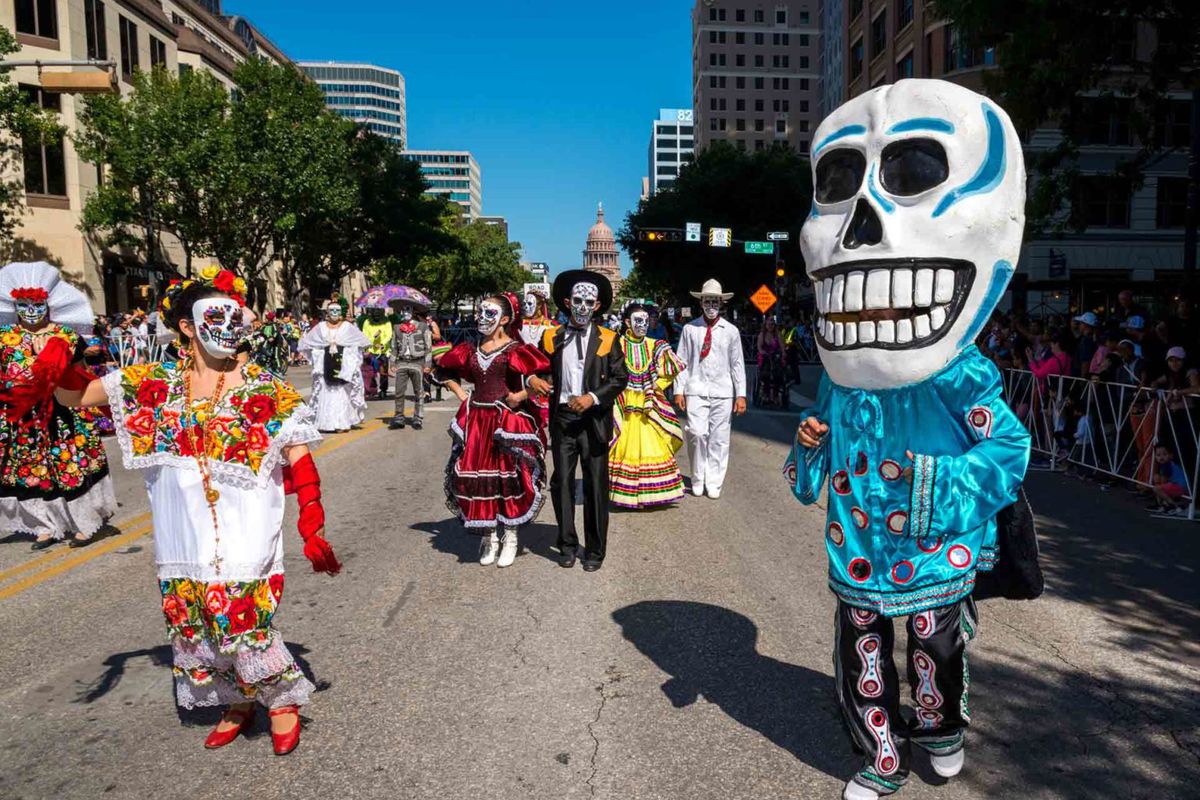 People on the street wearing skull masks and colorful outfits.