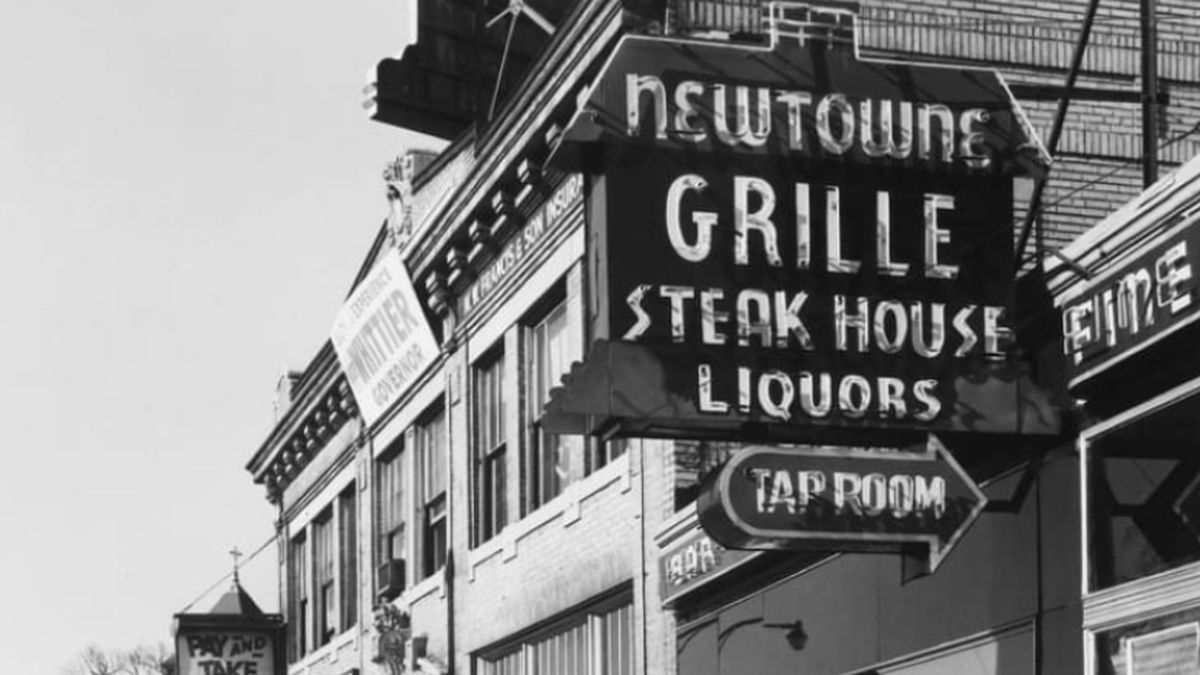 A black and white photo of Newtowne Grille in Porter square, taken in the 1960s. The sign reads, “Newtowne Grille: Steakhouse, Liquors, Tap Room.”