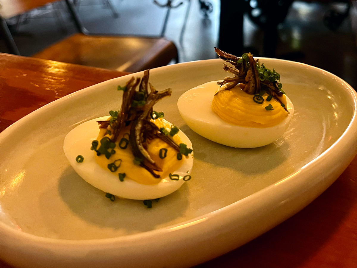 Eggs topped with anchovies, set in a sun-lit dining room where customers sit at the bar. 