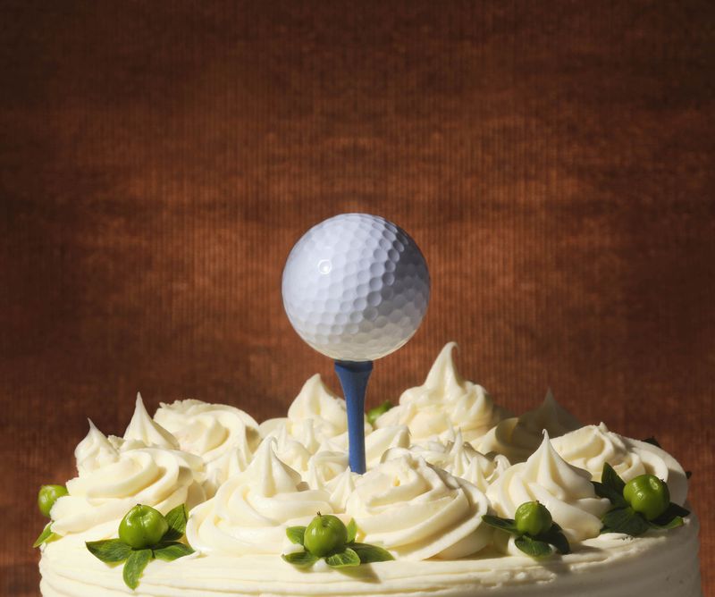 A white-frosted cake topped with a golf tee and golf ball. 