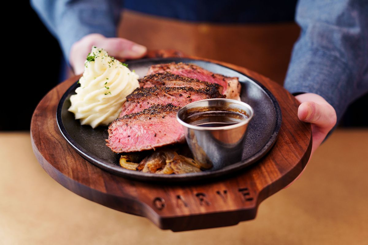 A black cast-iron plate of sliced steak, whipped mashed potatoes, and caramelized onions. 