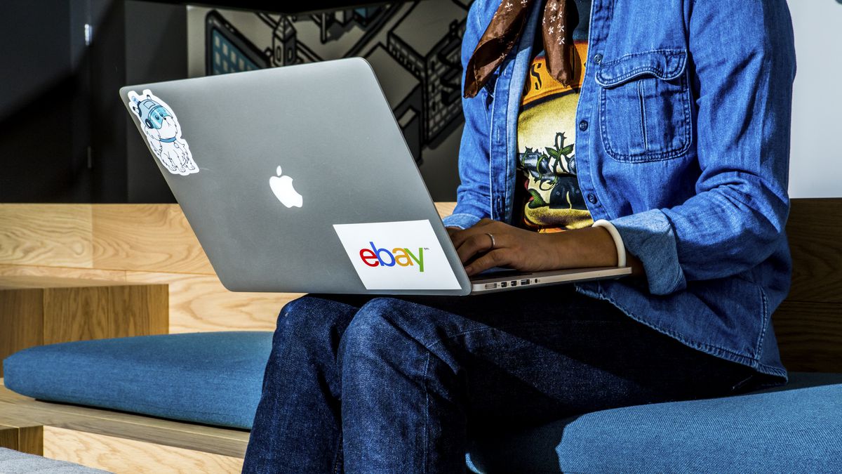 Woman sits with laptop on her lap. The laptop has an eBay sticker.