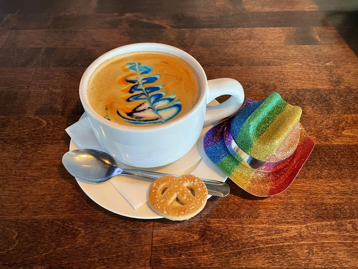 A rainbow latte beside a tiny glittery rainbow cowboy hat.
