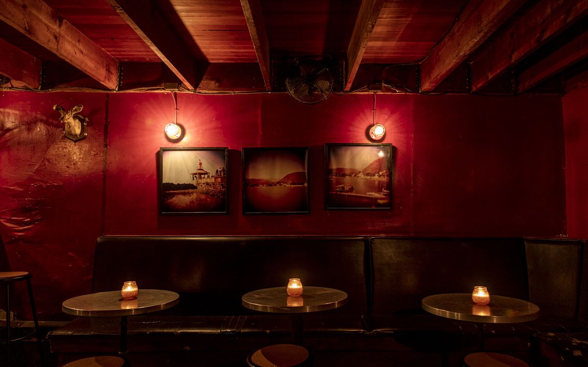 A view of the red walls inside the Hideout with round tables and two painting hanging above.