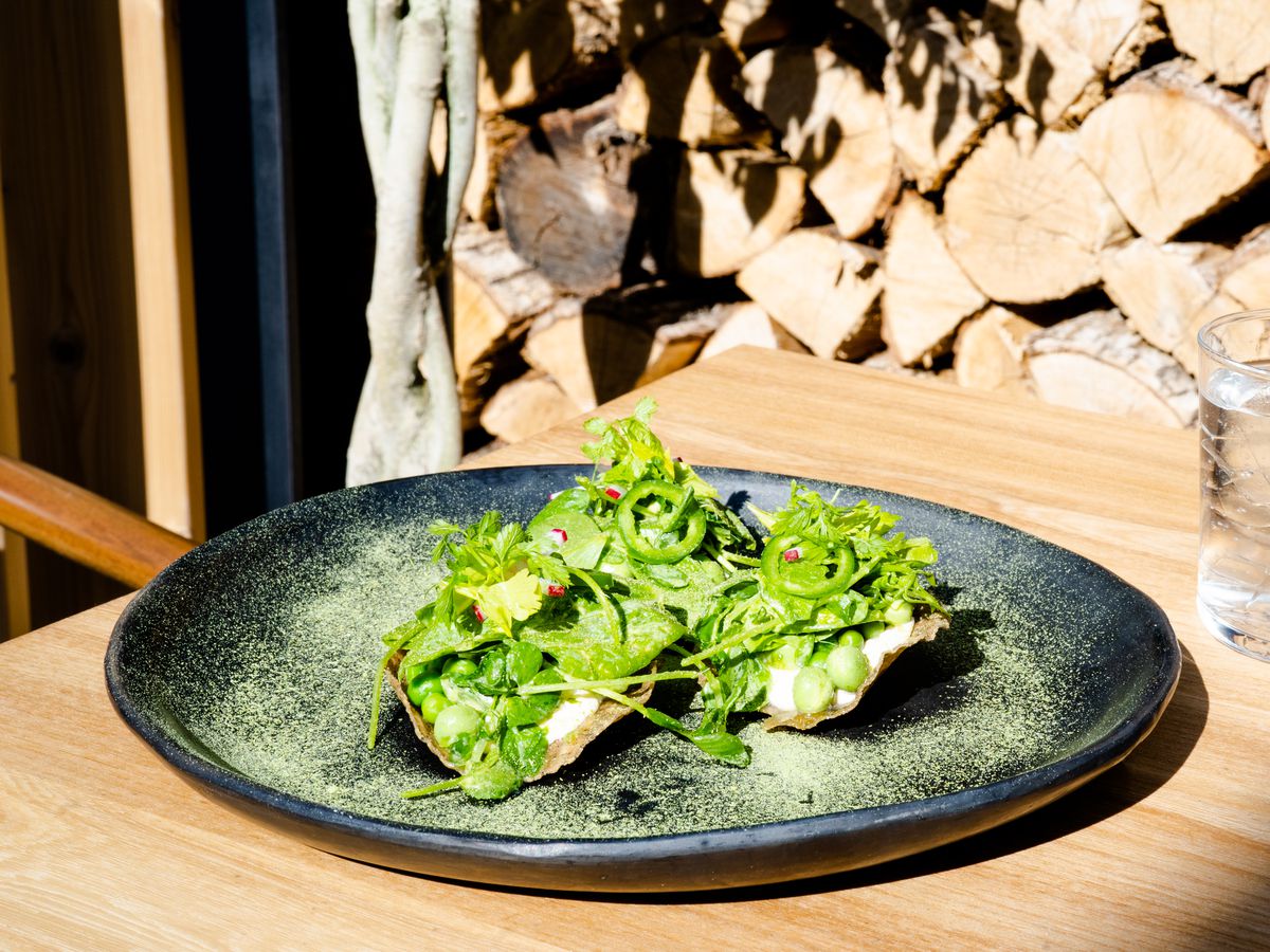 Crispy tortillas topped with cream, peas, greens, and jalapenos in a black dish on a wooden table. 