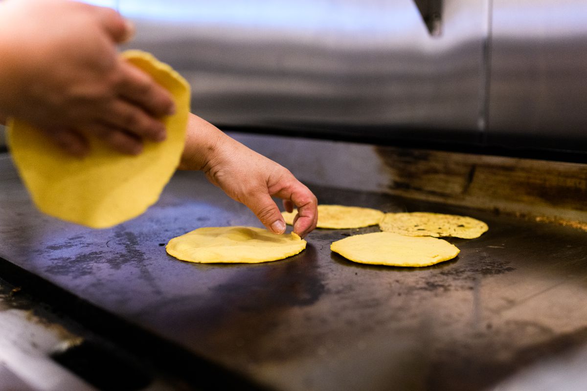 A picture of a cook at Papi Chulo’s placing five yellow corn tortillas on the griddle
