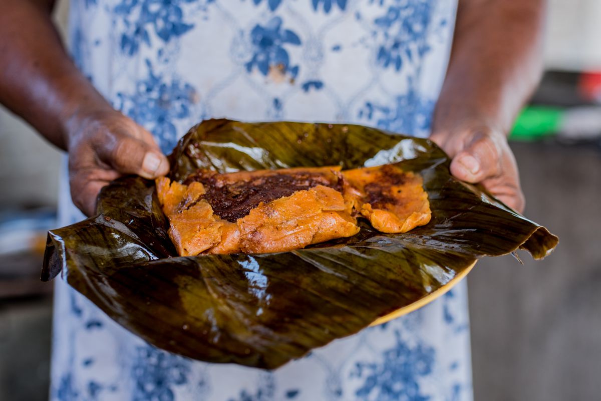 A pair of hands shows an unwrapped banana leaf tamale. 