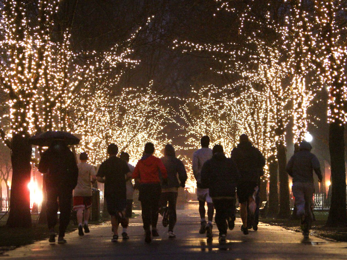 People running in a clump through the night between two lines of a lighted-up trees.