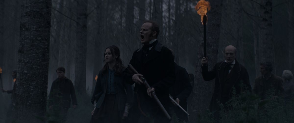 Alistair Petrie and a group of other men with rifles hunt a monster through the dark woods in The Cursed