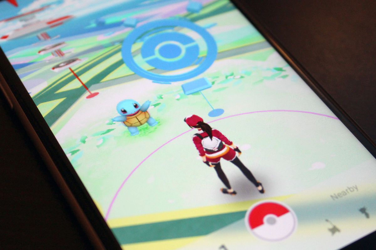 A photo of a phone with a Pokémon Go trainer standing in front of a PokéStop on the screen