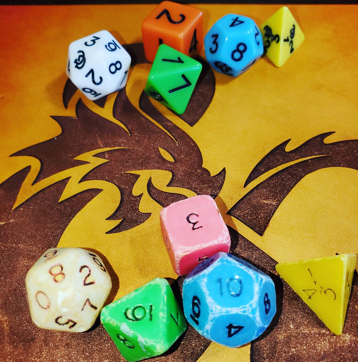 a set of colorful Dungeons &amp; Dragons dice on a table with a dragon on it