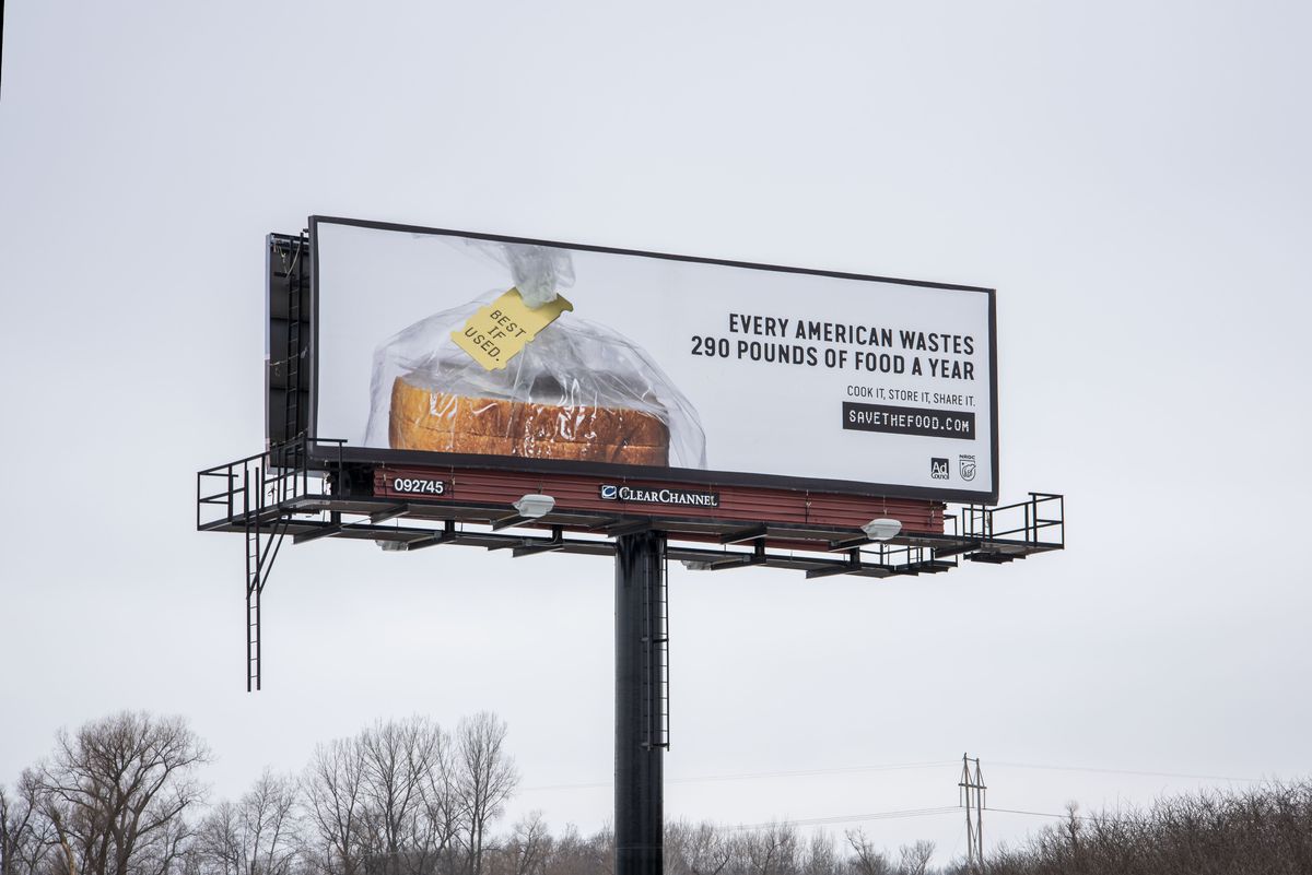 A billboard with a picture of a bagged loaf of bread reads, “Every American wastes 290 pounds of food a year. Cook it, Store it, Share it. Savethefood.com.” The tag on the bread reads, “Best if used.”