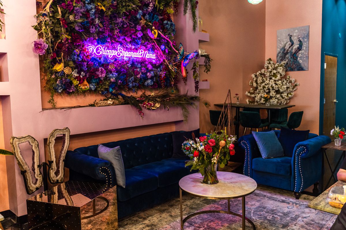 A corner of a restaurant space with blue velvet couches and lots of floral decorations.