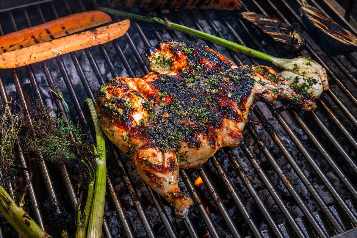 A charred, split chicken cooks on a wood-fired grill at L’Ardente.