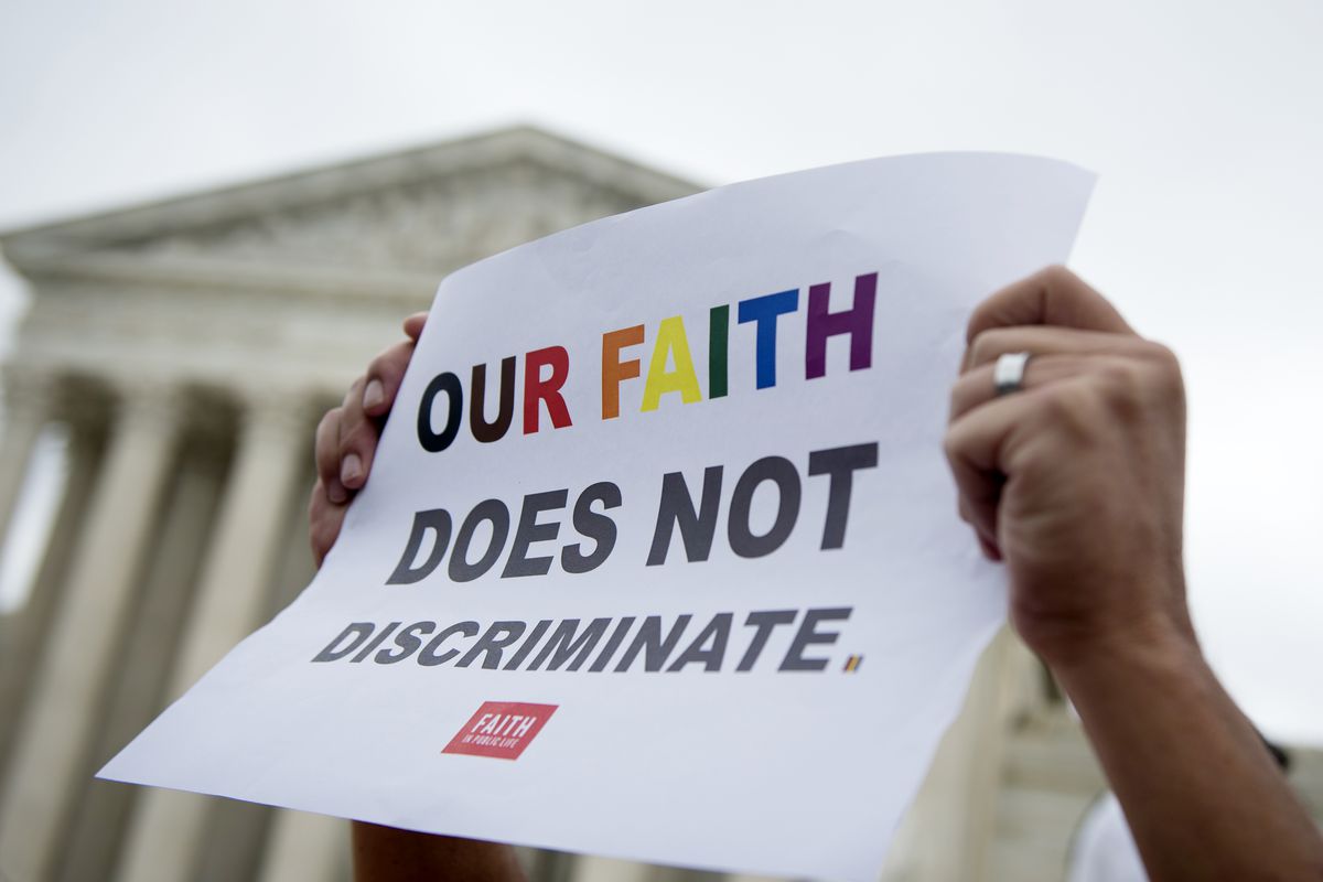 An arm holds up a sign saying “Our faith does not discriminate” in rainbow-colored letters, in front of the US Supreme Court building.