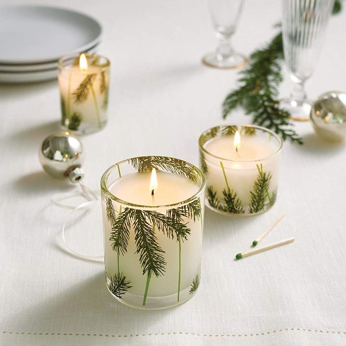 Two jar candles with evergreen print on the containers sit on a table. 