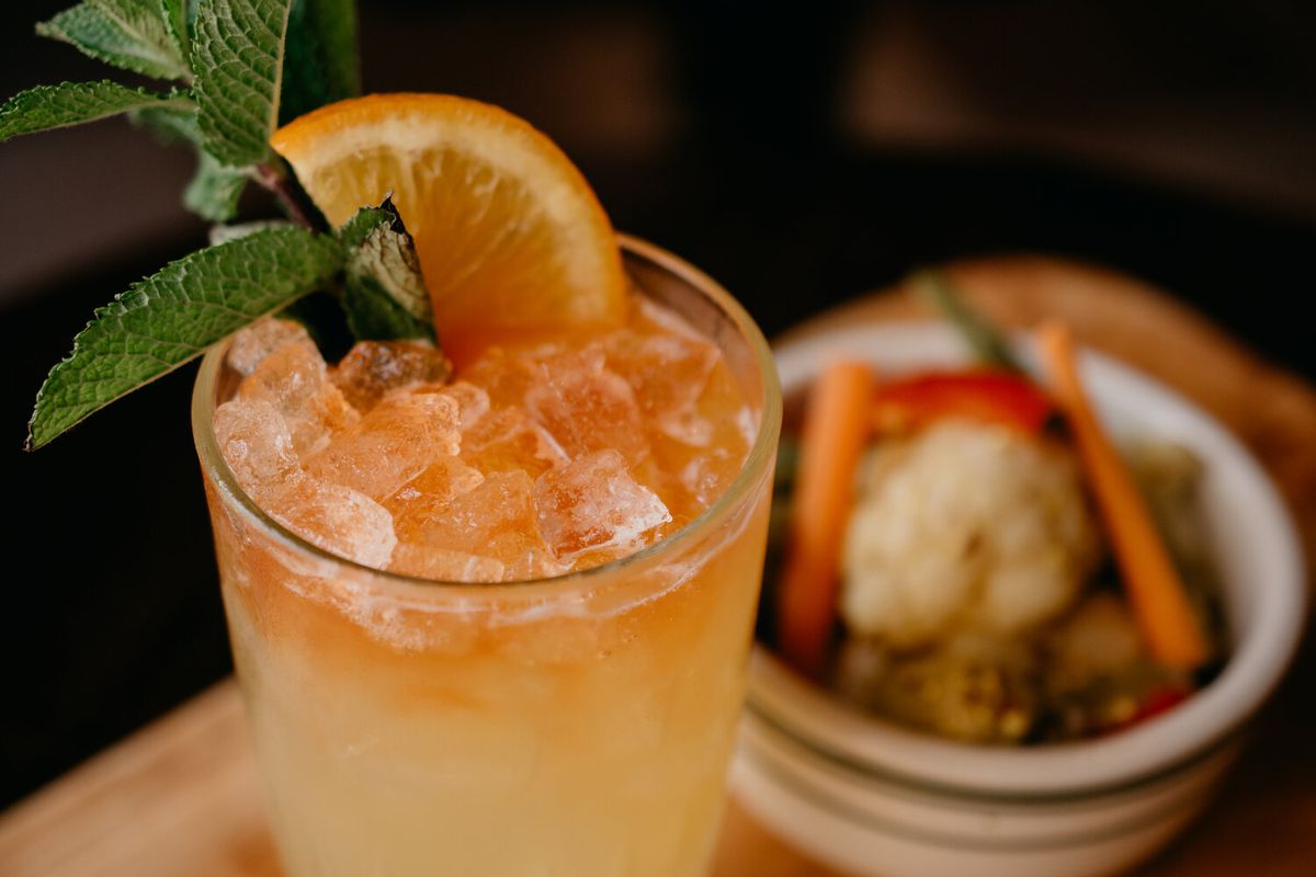An orange cocktail with a mint sprig and slice of orange and ice. 