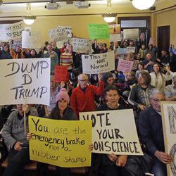 Protesters hold signs as Utah's six presidential electors prepare to cast their votes for President-elect Donald Trump, Monday, Dec. 19, 2016, in Salt Lake City. The six electors, who were chosen by Utah GOP delegates earlier in the year, cast their votes in a brief meeting Monday at the state Capitol as protesters filled the room, yelling "Vote your conscience," and "The whole world is watching."