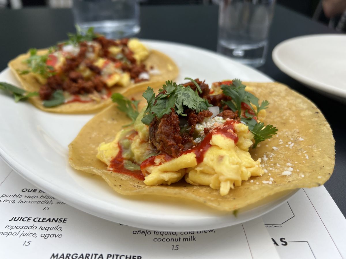 Light yellow scrambled eggs sit on two corn tortillas garnished with green cilantro and red chorizo
