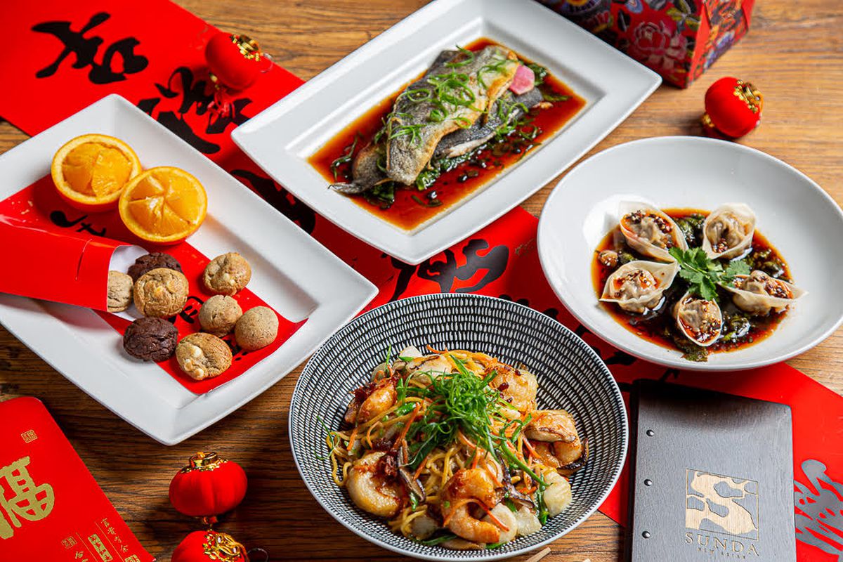 Dumplings, whole fish, and shrimp on various white plates on bright red menus with Asian script 