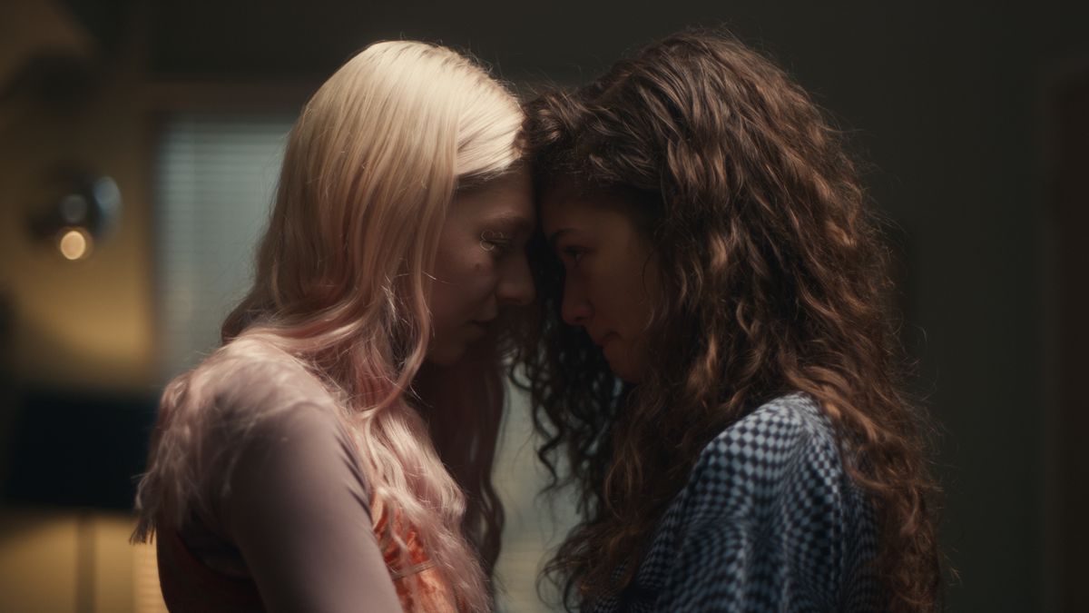 Two girls — one with soft blond hair and pink highlights, and the other with dark, curly brown hair — press their foreheads together on Euphoria