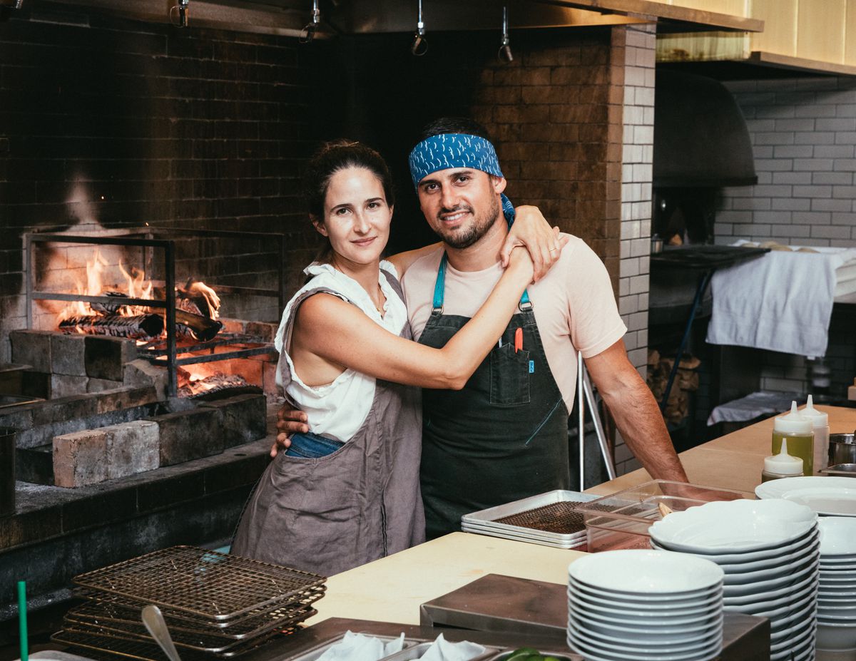 A chef owner couple in front of a live fire in a restaurant.