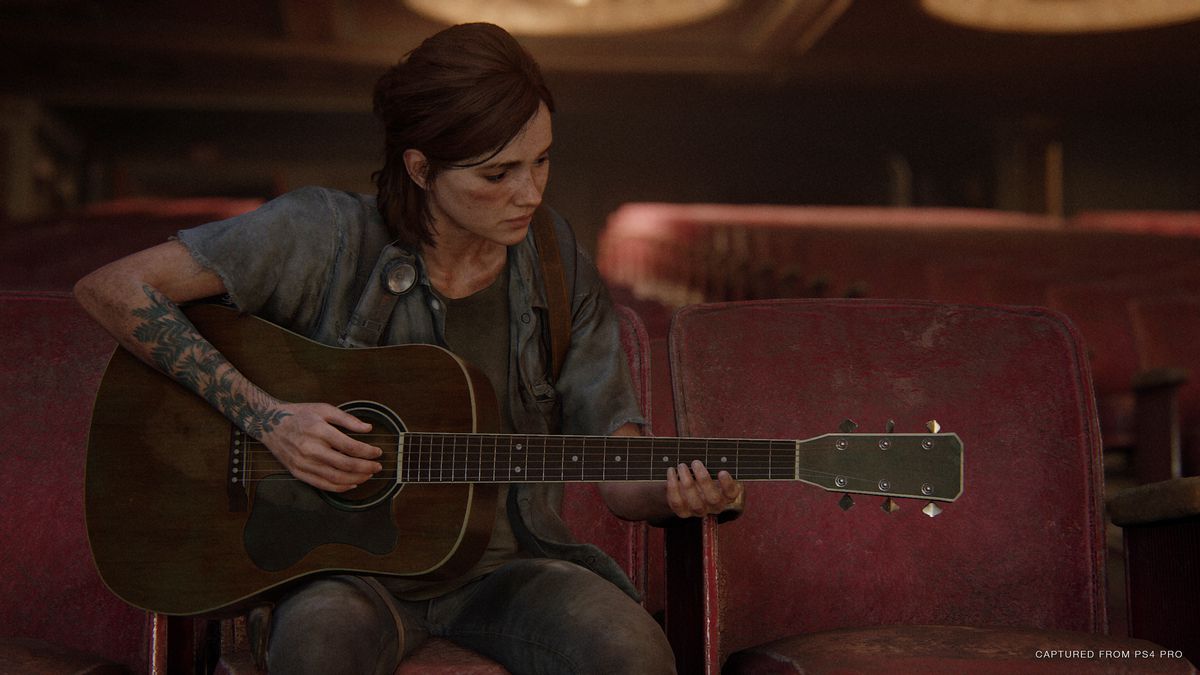 Ellie seated in the audience of a theater, playing the guitar in The Last of Us Part 2