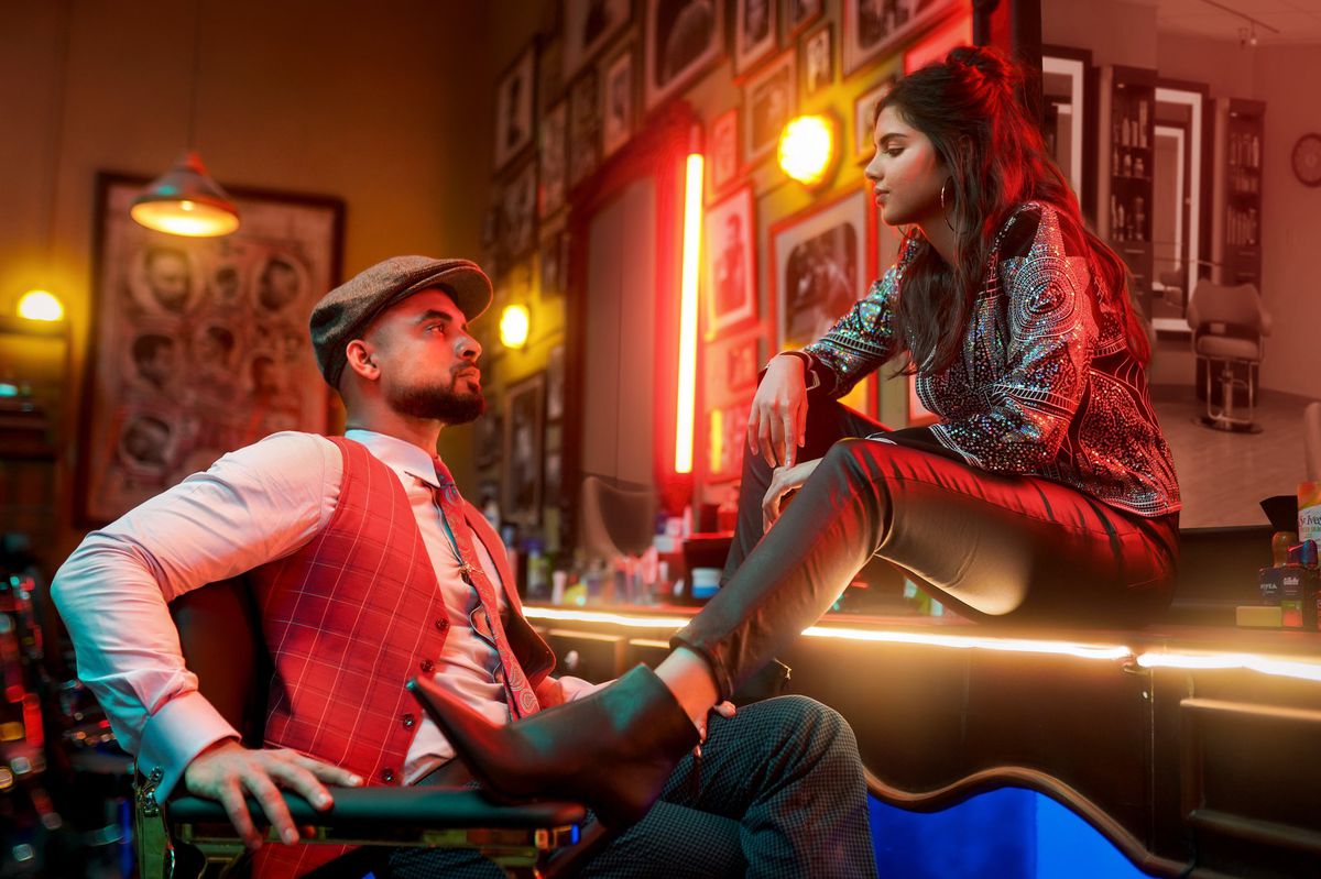 Tovino Thomas and Kalyani Priyadarshan face each other in a barber shop in Thallumaala. She sits on a counter, with her left leg on the right arm of the chair he sits in, while they look at each other.