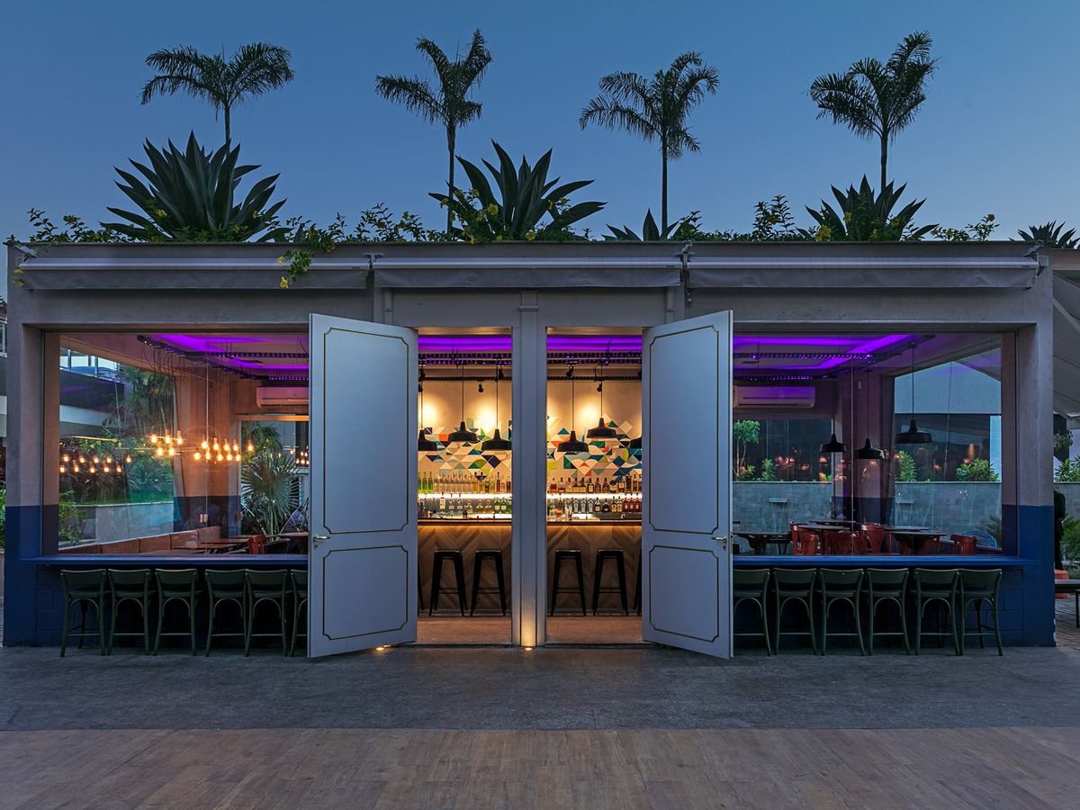 A restaurant exterior at night with palm trees swaying above.