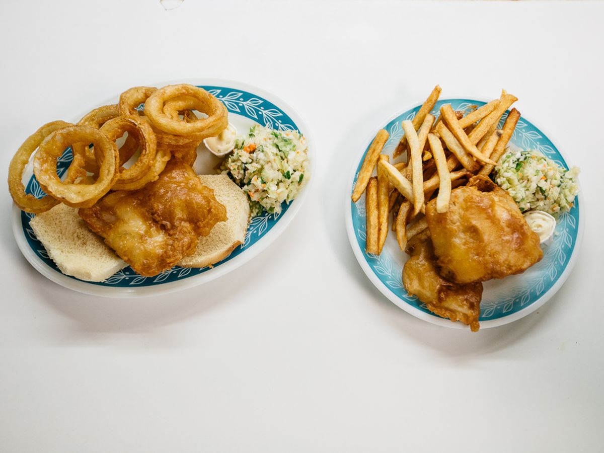 Two blue and white patterned plates filled with fish and chips, coleslaw, rolls, fries, and onion rings.