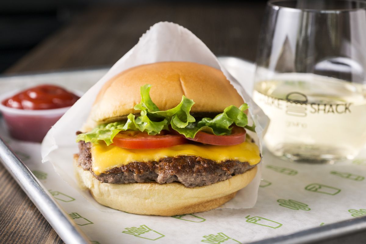 A picturesque Shake Shack smash burger with cheddar cheese, tomatoes, and lettuce.