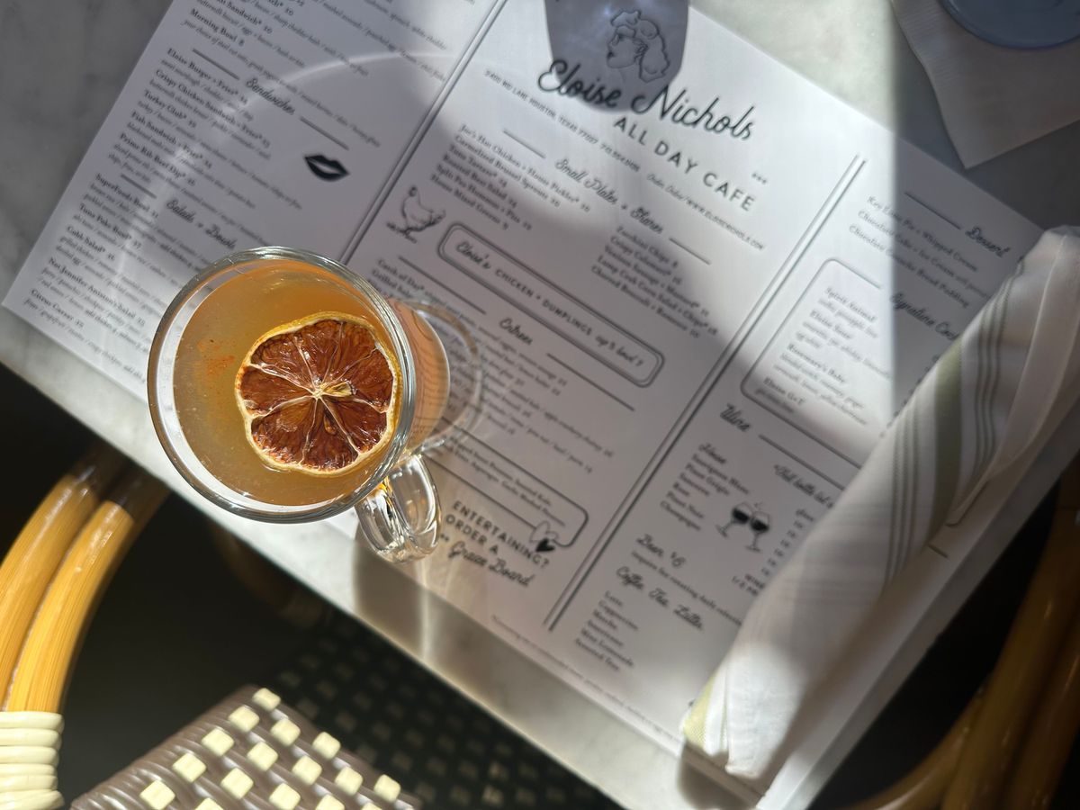 An overhead shot of the Eloise Hot Toddy, made with Four Roses Bourbon, lemon, turbinado, and cinnamon, and garnished with a lemon slice, sitting on top of a menu.