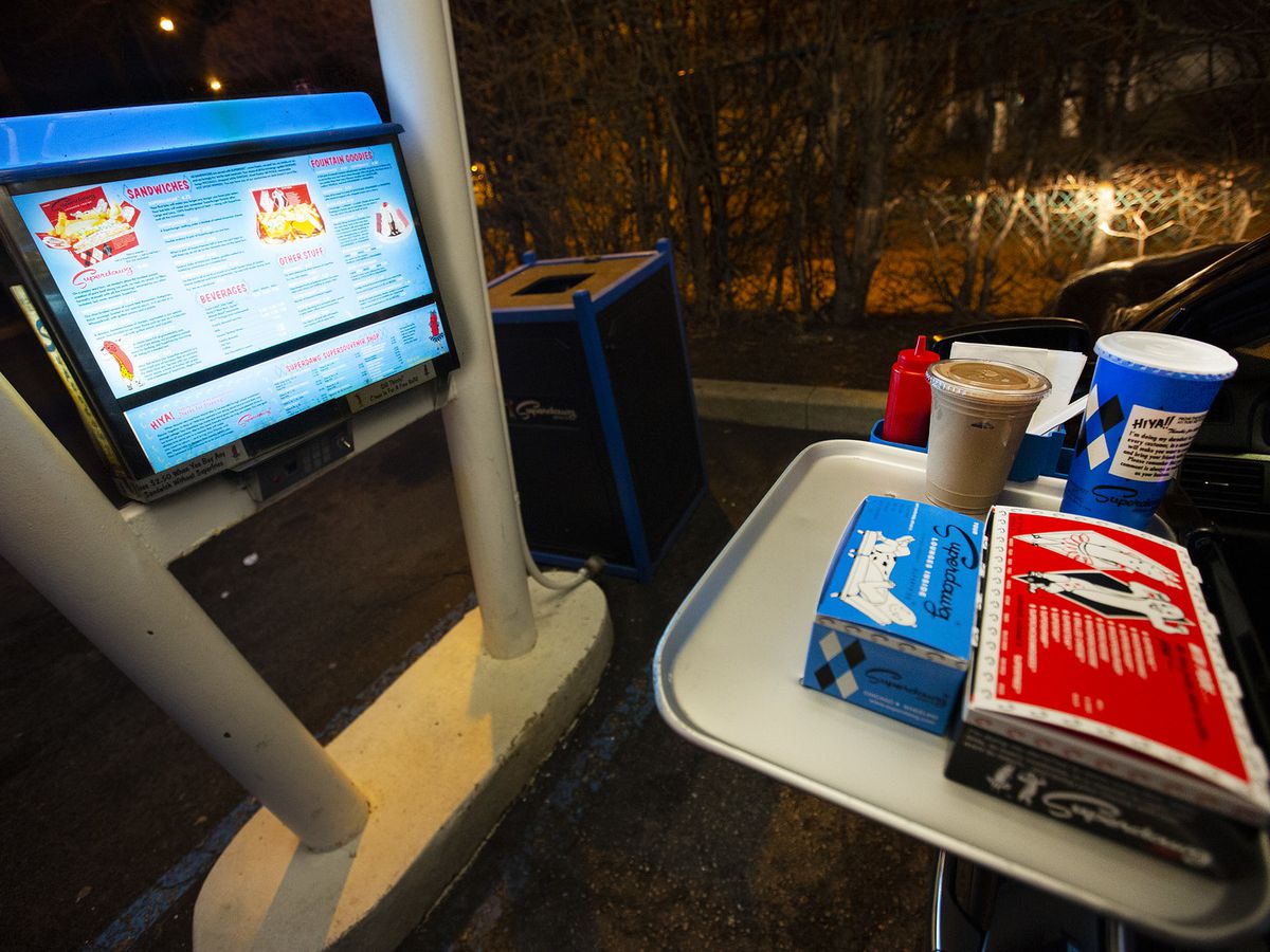 A carhop with tray of food hanging from a door and drive-in menu.
