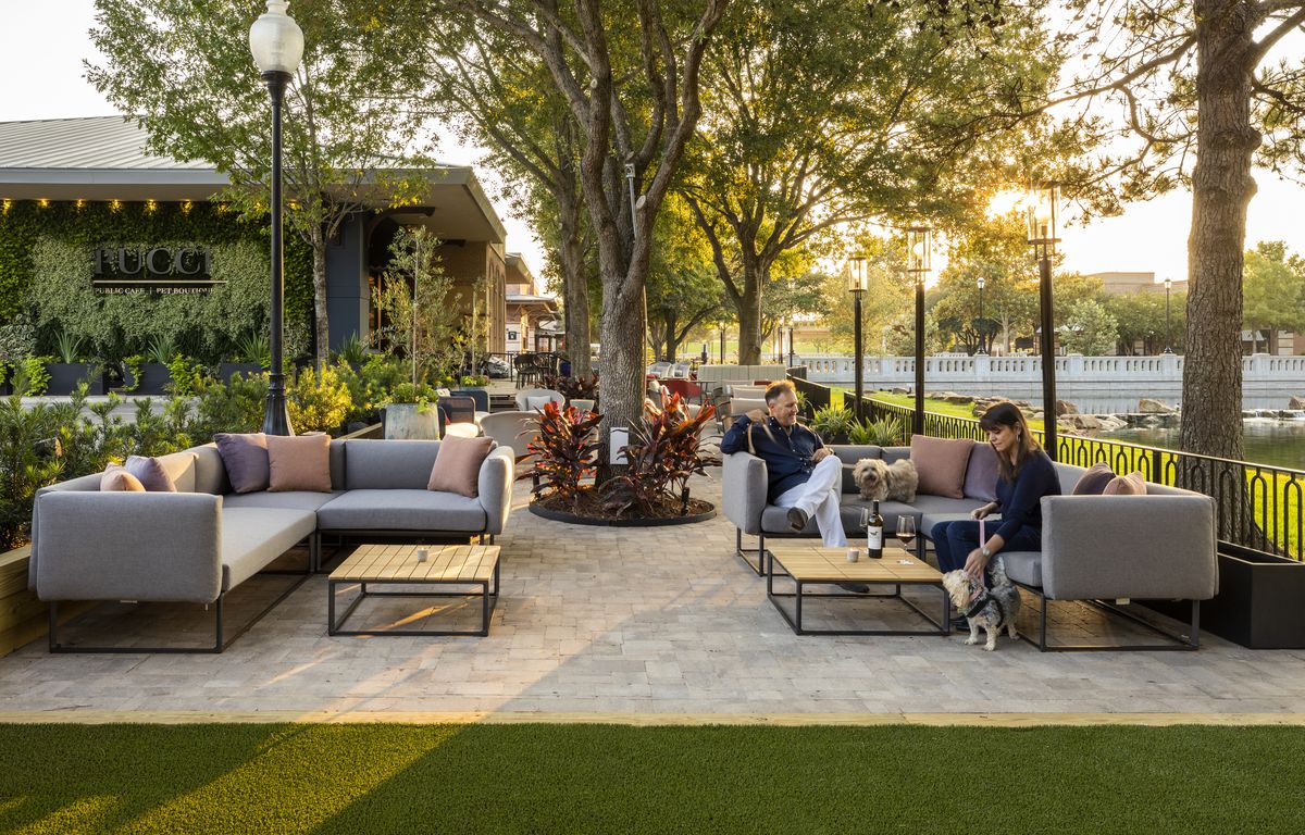 A woman and man playing with a dog on a patio, outfitted with various couches, chairs, and trees at La Pucci’s.