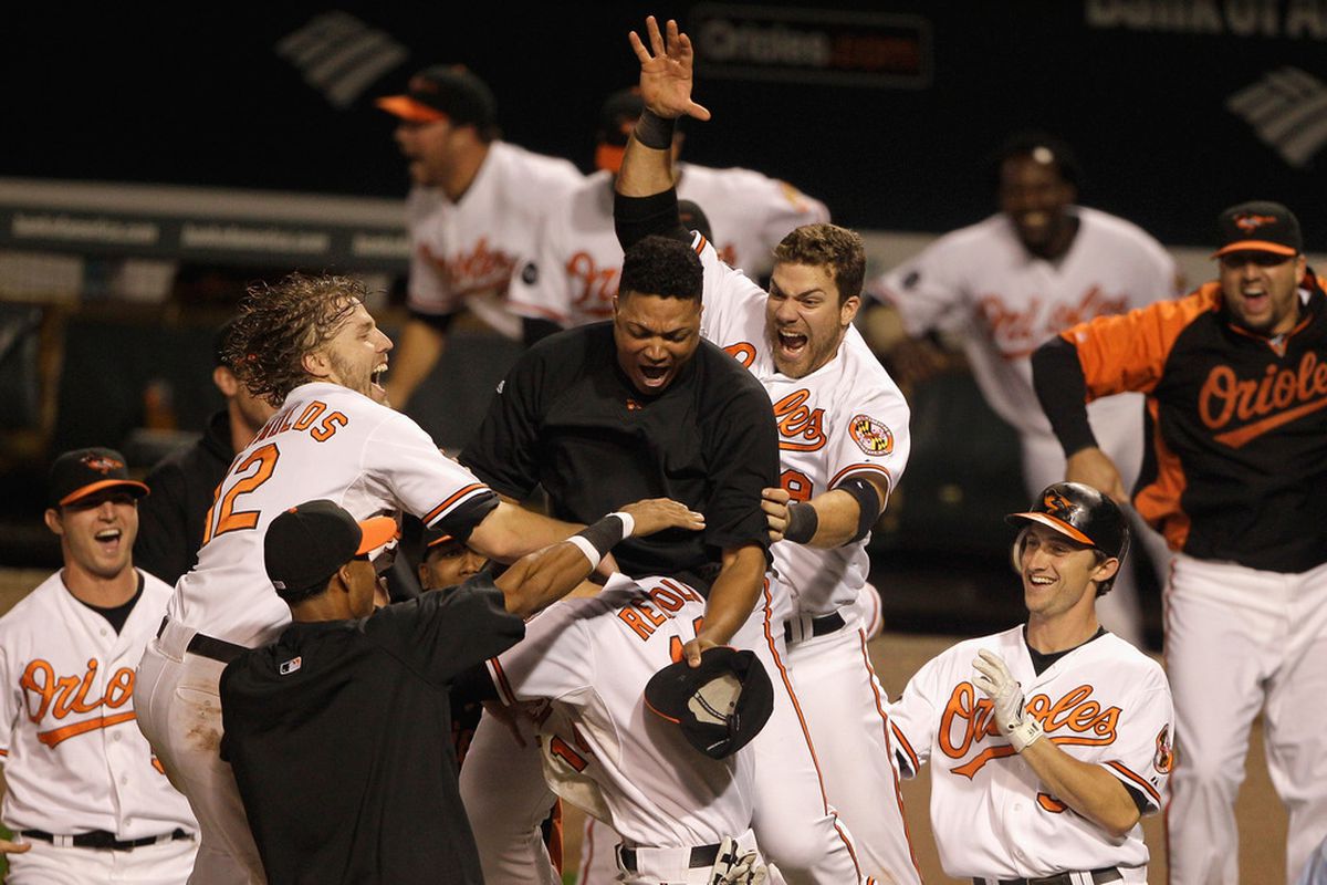 Members of the Baltimore Orioles swarm Nolan Reimold after he scored the winning run to defeat the Boston Red Sox 4-3 at Oriole Park at Camden Yards on September 28, 2011 in Baltimore, Maryland.  (Photo by Rob Carr/Getty Images)