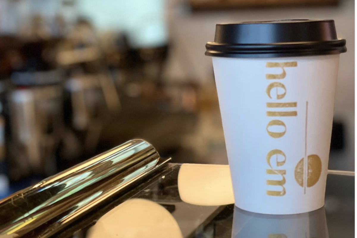 A paper cup that says “Hello Em” in gold lettering on a cafe counter