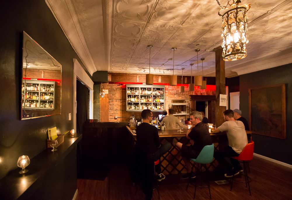 The dark interior of Mudgie’s wine bar features three customers sitting in blue and red upholstered bar stools.