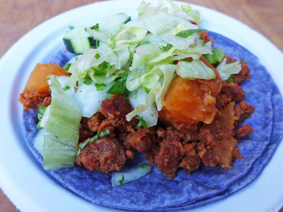 Crumbled sausage and orange potato cubes on a pair of soft bright blue corn tortillas.
